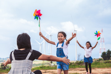 Two asian child girls playing with wind turbine toy and running to their mother to give a hug in...