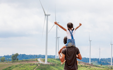Fototapeta na wymiar Father and daughter having fun to play together. Asian child girl riding on father's shoulders in the wind turbine field