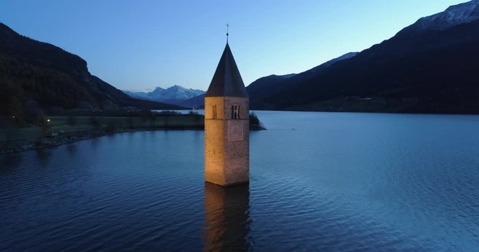 Aerial: Slow Pan of the Picturesque Bell Tower of Lake Reschen at Night with Backdrop of Alps - South Tyrol, Italy