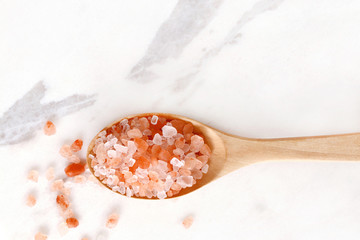 top view of himalayan pink salt in wooden spoon on white marble table.