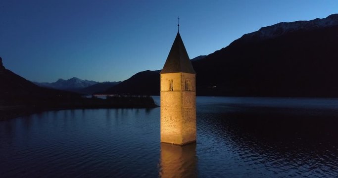 Ascending Aerial: The Submerged Bell Tower of Lake Reschen at Night Against the Backdrop of Dark Hills - South Tyrol, Italy