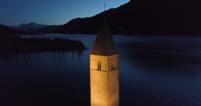 Aerial Pan: Bell Tower of Lake Reschen at Night With Backdrop of Dark Hills and Mountains - South Tyrol, Italy
