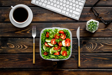 meal in lunch box and coffee for dinner on wooden office desk background with keyboard top view