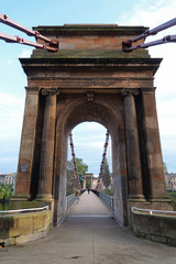 Obraz premium The historic South Portland Street Suspension Bridge of Glasgow, Scotland is shown in a vertical view during the day. The pedestrian footbridge, which crosses River Clyde, was completed in 1853 and is