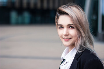 Happy European young business woman in formal clothes. Businesswoman in a jacket and white shirt smiling. Workplace, outdoor. Girl is looking at camera with cheerful confident expression. Copy space. 