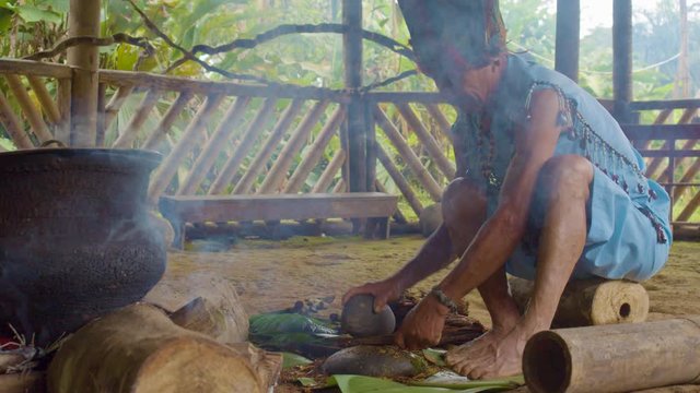 Indigenous Man Crushing Ayahuasca Sticks To Prepare Traditional Drink In The Amazon Rainforest In Ecuador