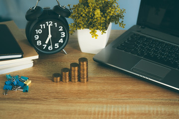 Coin stack and financial graph paper sheet with notebook calculator and alarm clock on working table for business concept.
