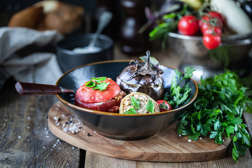 Baked eggplant or eggplant stuffed with pork and beef, peppers, tomato and fresh parsley in a black plate on a wooden table
