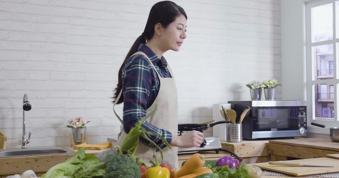 beautiful household woman in kitchen smiling look vegetables while double checks ingredients and instructions on digital tablet. young girl in apron prepare cooking for family in day city apartment.