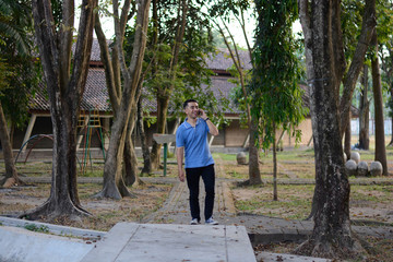 Portrait of handsome Asian male in blue t-shirt talk at phone in outdoor parks