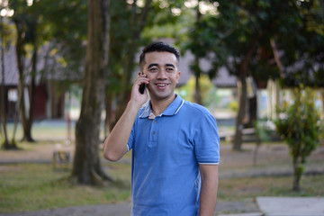 Portrait of handsome Asian male in blue t-shirt talk at phone in outdoor parks