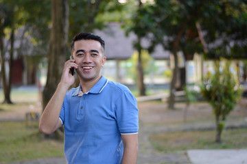 Portrait of handsome Asian male in blue t-shirt talk at phone in outdoor parks