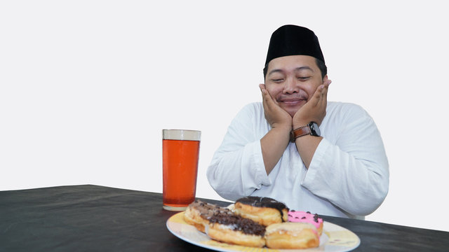 Portrait of overweight muslim man with head cap or songkok pray before eat and drink for islam break fasting