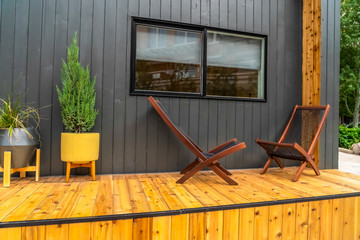 Wooden chairs on the porch of a home in front of a gray wall and sliding window