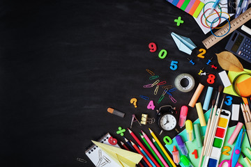 Set of stationery, alarm clock and supplies on blackboard background. Back to school concept. Top view.
