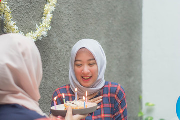 attractive hijab woman having surprise birthday cake from her bestfriend with candle while sitting on cafe