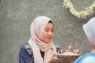attractive hijab woman having surprise birthday cake from her bestfriend with candle while sitting...