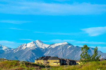 Fototapeta premium Houses on a hill overlooking snowy mountain peak against cloudy blue sky