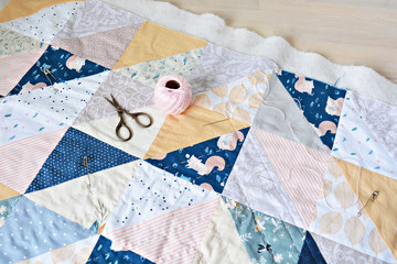 Hand stitch quilting process: pink cotton thread, needle and scissors on the table	