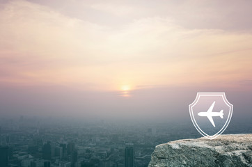 Airplane with shield flat icon on rock mountain over aerial view of cityscape at sunset, vintage style, Business travel insurance and safety concept