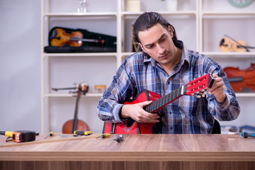 Young handsome repairman repairing guitar