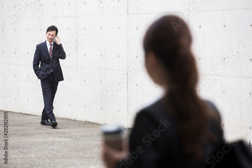 電話をしながら歩くスーツ姿の男性とすれ違う女性 Wall Mural Uts