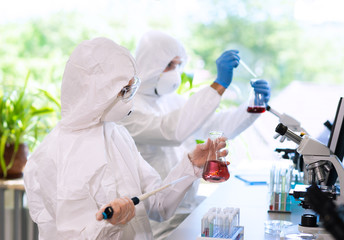 Scientists in protection suits and masks working in research lab using laboratory equipment:...