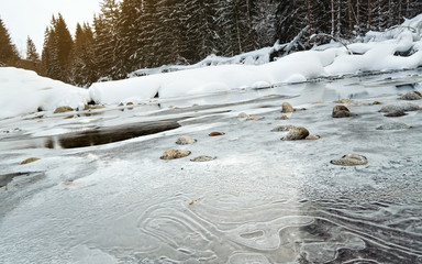 Morning on frozen river in winter, low angle photo, focus on ice patterns and stones, with...