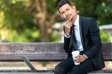 Malay Business man working on his laptop during his coffee break at the park.