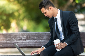 Malay Business man working on his laptop during his coffee break at the park.