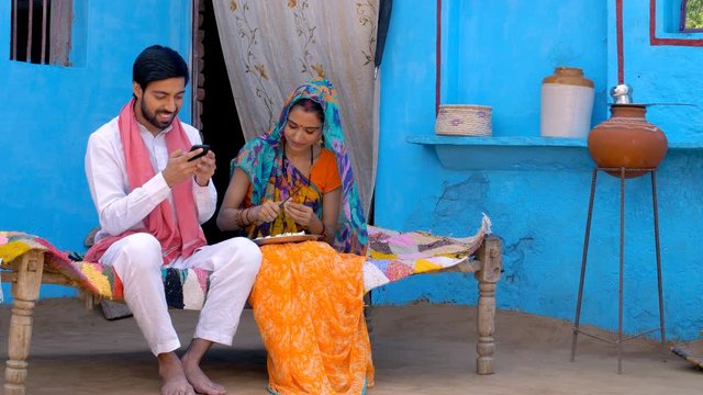 Young attractive husband showing new things to his beautiful wife on his new smartphone - Village life. Village scene of an Indian farmer and his wife showing new things on his mobile phone  smilin...