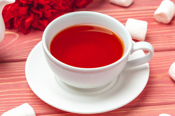 Obraz premium Cup of tea with sweets and flowers on wooden table