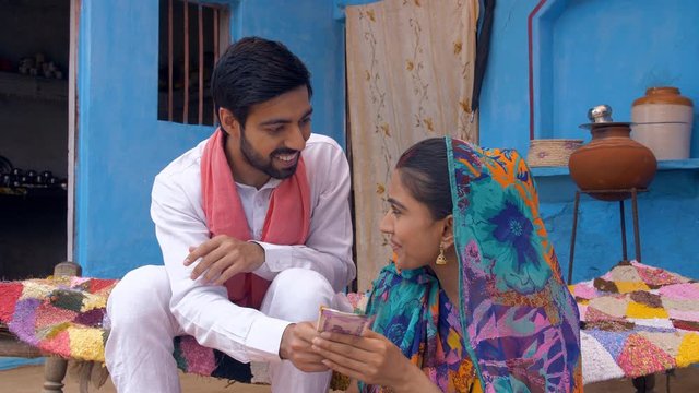 Young good looking village husband giving Indian rupee notes to his wife - future investment . Indian villager happily giving his monthly salary to his beautiful wife - village life in India