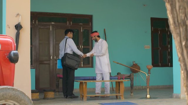 Indian government employee approaching villagers to inform about new policies. Young Indian farmer welcoming government official to his house  shaking hands and asking him to sit on a charpai