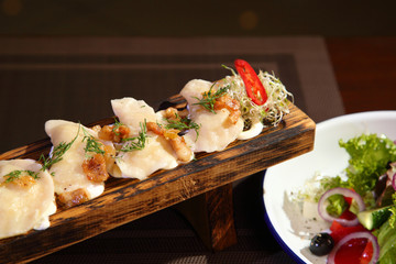 Dumplings with potatoes and greaves in sour cream on a wooden board and salad. Dumplings with potatoes and salad.
