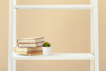 White bookshelf with  books and stationery against beige wall