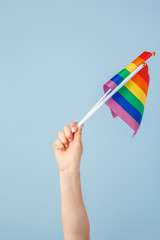 Closeup of a hand waving a small rainbow flag against a light blue background