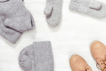 Autumn or winter female outfit. Set of clothes and shoes on white background. Warm knitted cap, mittens and snood or scarf grey colored, leather orange boots. View from above. Copy space.