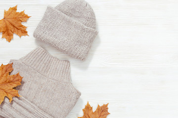Fototapeta na wymiar Autumn flat lay with warm clothing. Fashion clothes for womans woolen grey knitted jumper and beautiful cap on white wood with copy space. Top view. Flat lay.