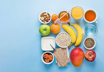Healthy whole food fiber source breakfast with rolled oats honey fruits apples banana citrus mango orange juice water herbal tea nuts on blue tabletop. Vegan plant based diet healthy lifestyle