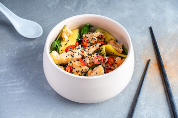 Thai styled bowl salad on grey stone background. Warm salad with sweet and sour chicken, pepper chili, mango, spinach. Copy space for design. Flat lay pam-asian food