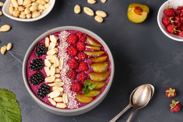 Healthy breakfast smoothie bowl with blackberries, plums, raspberries, peanuts and sesame seeds on a dark background, horizontal photo
