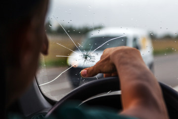 Broken windshield of a car. A web of radial splits, cracks on the triplex windshield. Broken car windshield, damaged glass with traces of oncoming stone on road or from bullet trace in car glass