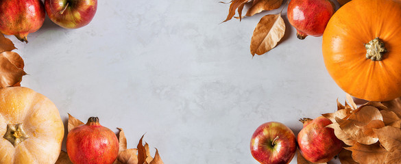 Orange and peachy pumpkins ripe organic red glossy apples pomegranates chestnuts dry golden autumn leaves on gray marble stone background. Thanksgiving fall harvest abundance. Long banner copy space