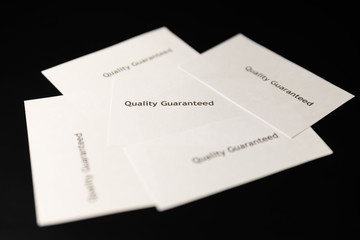 Five notes with words "Quality Guaranteed" are on the black table/background.  World Quality Day