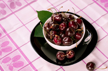 Juicy large dark cherry in a black plate, which stands on a wooden table