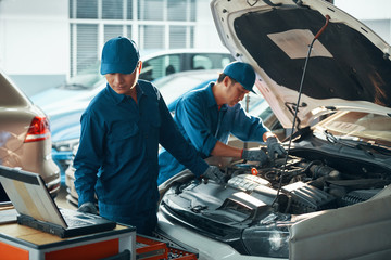 Team of Vietnamese mechanics using computer diagnostics system when checking car motor