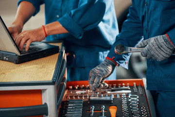 Mechanic searching for right size of wrench when his coworker making computer diagnisctics of car