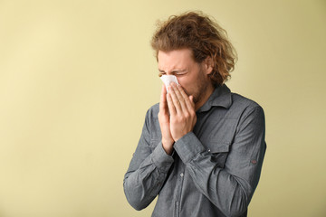 Sick young man with nose wiper on color background
