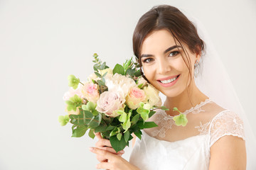 Naklejka premium Beautiful young bride with bouquet of flowers on light background
